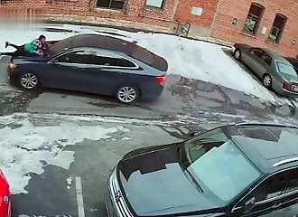A woman is carried off the hood of her car by a thief